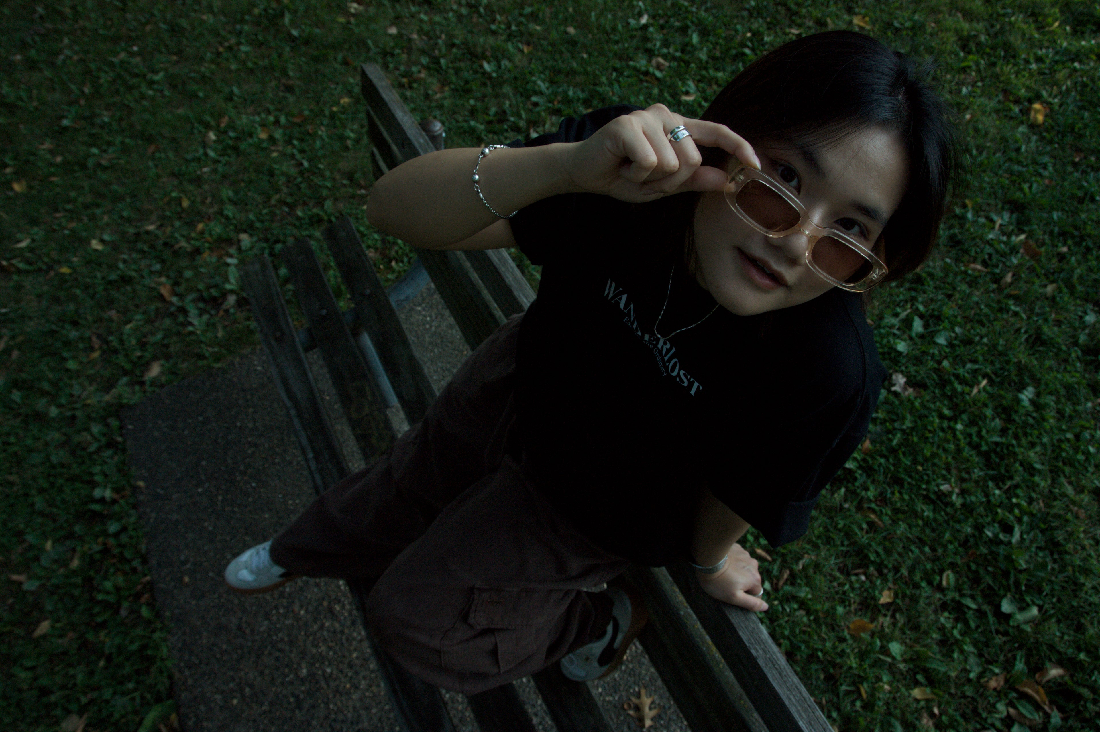 Person sitting on a bench in a park, wearing sunglasses and a black hoodie.